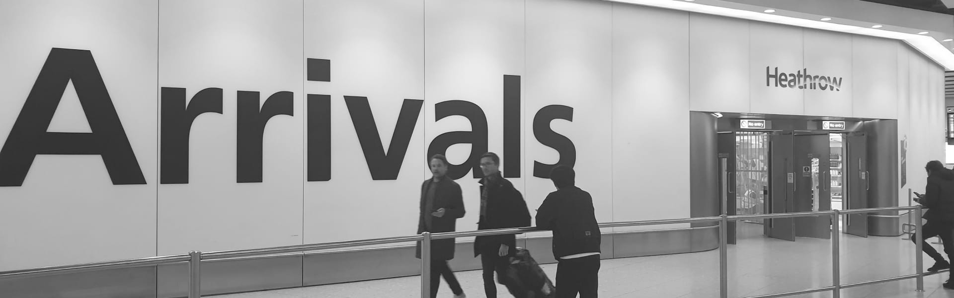 People walking out of the airport arrivals gate with 'Arrivals' written on the wall.