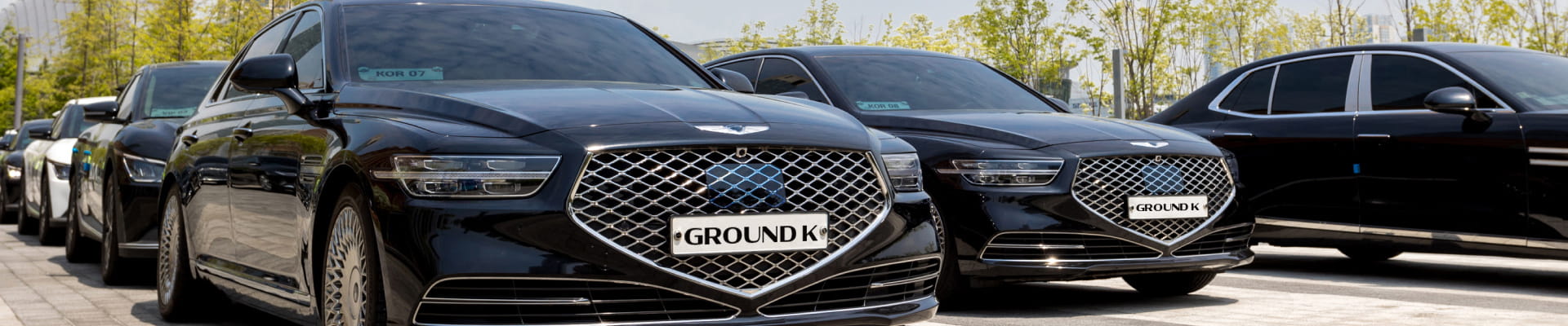 Luxury sedans with GroundK logo license plates parked in a row.