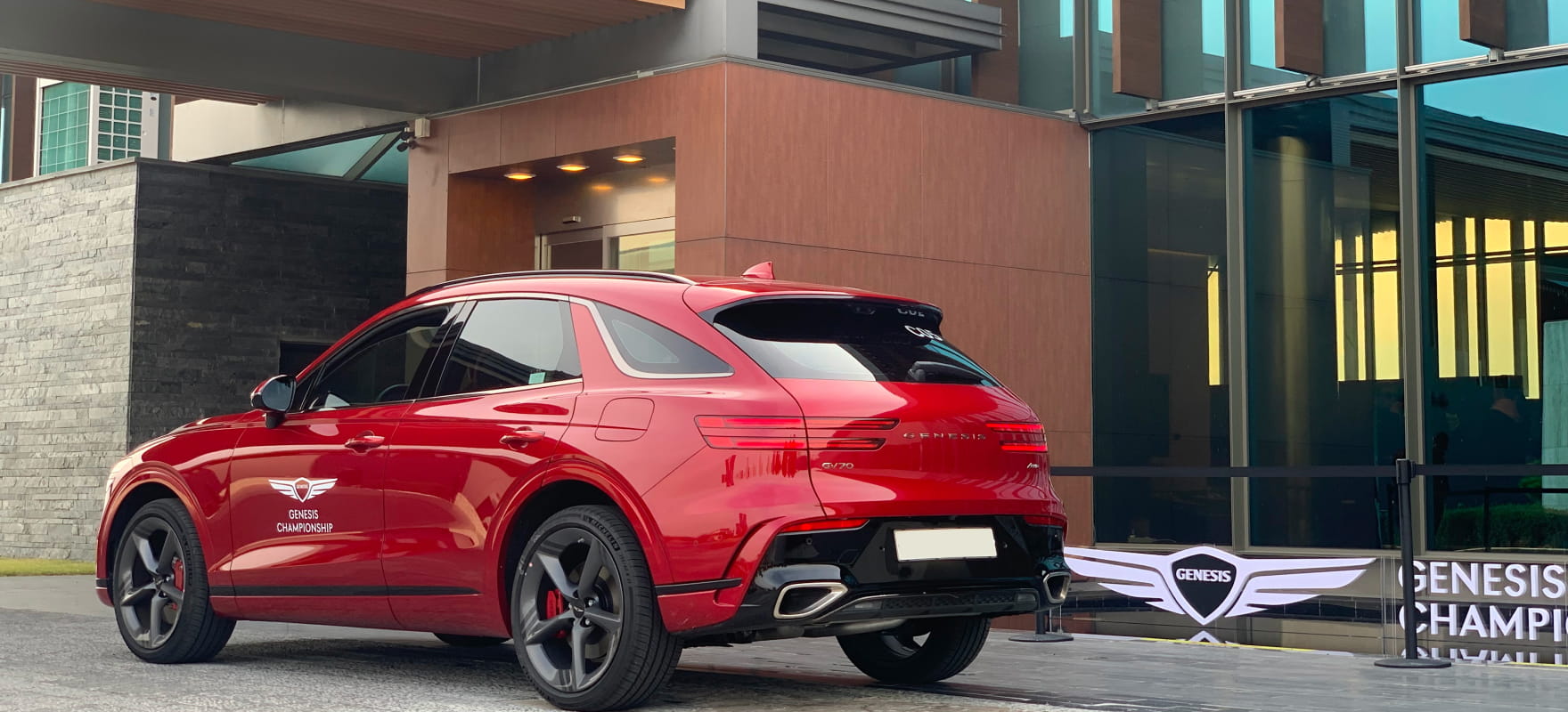 Rear side view of the official red Genesis GV70 SUV featuring the Genesis Championship logo and sleek tournament branding.
