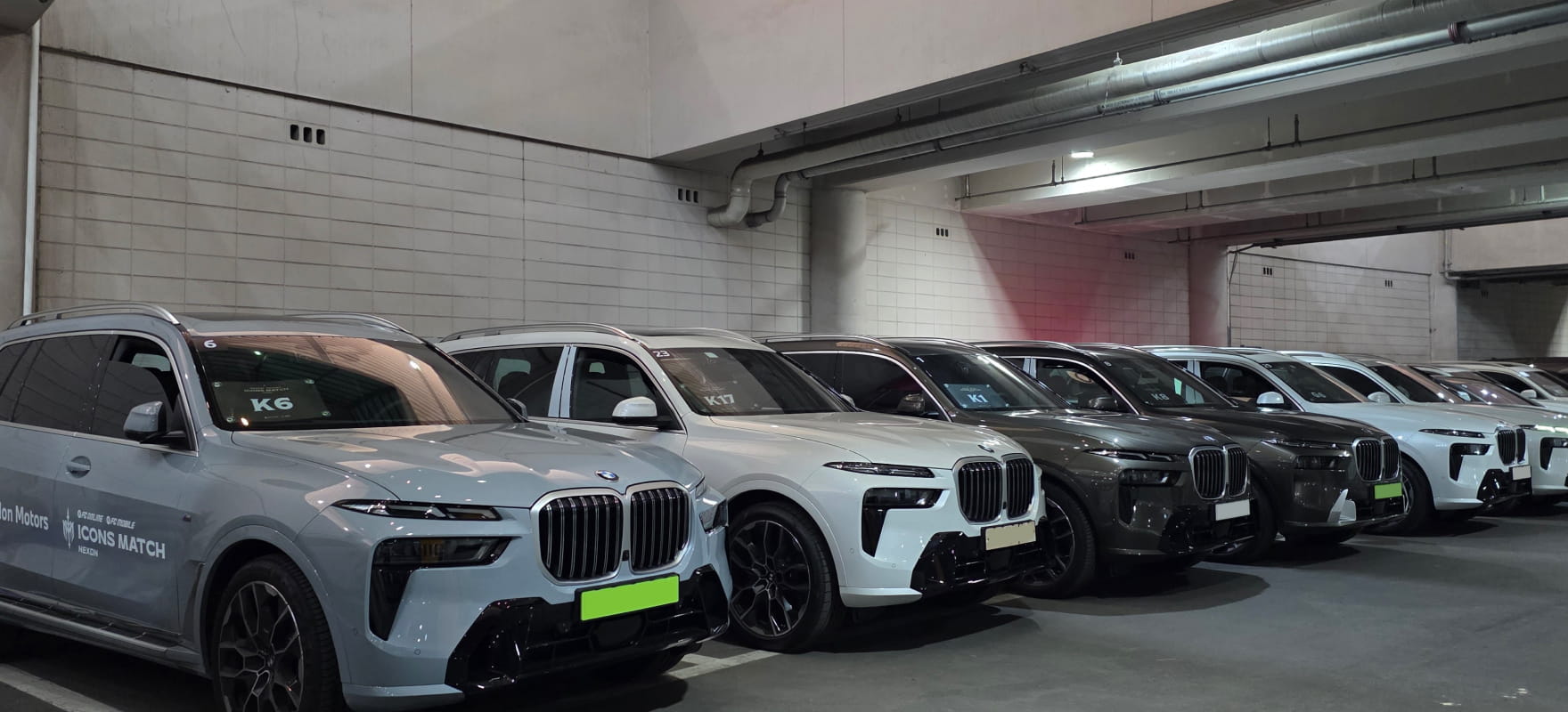 A fleet of BMW X7 SUVs with official event decals lined up in an underground parking facility, ready for coordinated dispatch.