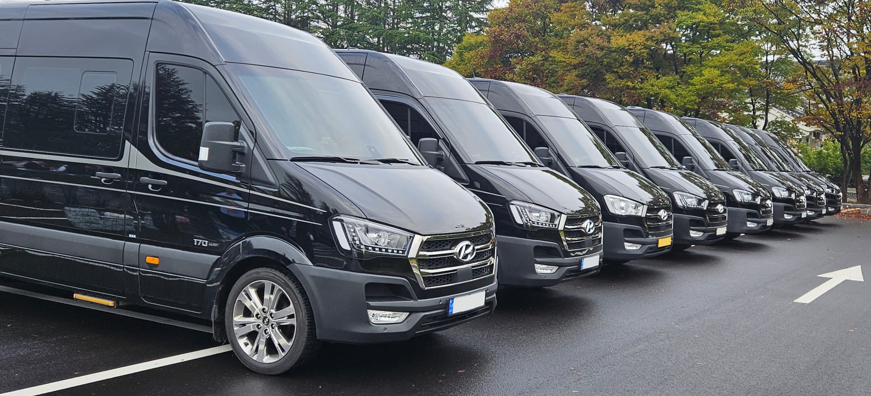 A line of black Hyundai Solati (H350) vans prepared for APEC summit shuttle operations, surrounded by autumn foliage.